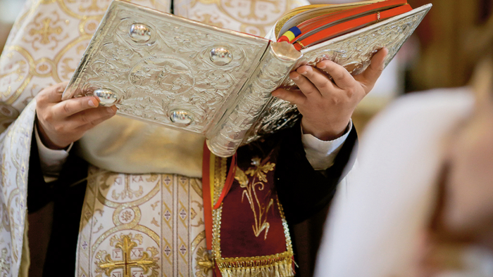 Bucharest, Romania - May 24, 2020: Details of an Orthodox priest reading from the Holy Bible during an Orthodox Baptism.